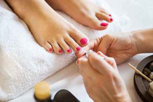 Woman in nail salon receiving pedicure by beautician. Close up of female feet resting on white towel