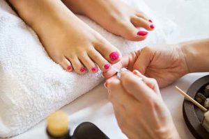 Woman in nail salon receiving pedicure by beautician. Close up of female feet resting on white towel