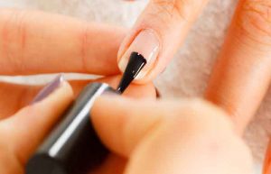 Closeup of beautician painting nails of female client. Woman in beauty spa salon doing manicure